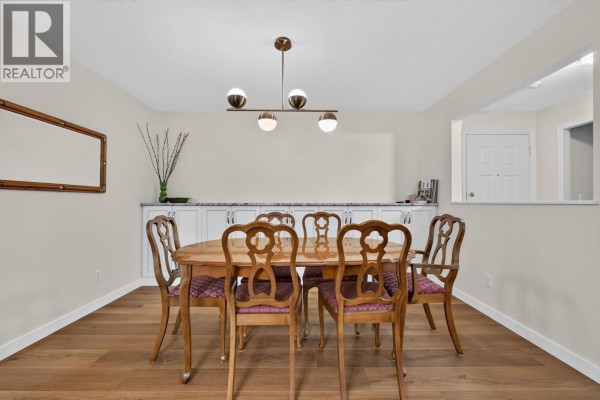 Dining room with a wooden table, six chairs, built-in cabinets, and a modern chandelier. - 920 Glenwood Avenue Unit# 208, Kelowna