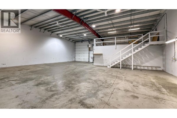 Exterior of a commercial building with three grey roll-up doors and a silver SUV parked outside. - 9207 James Avenue Unit# 103, Summerland