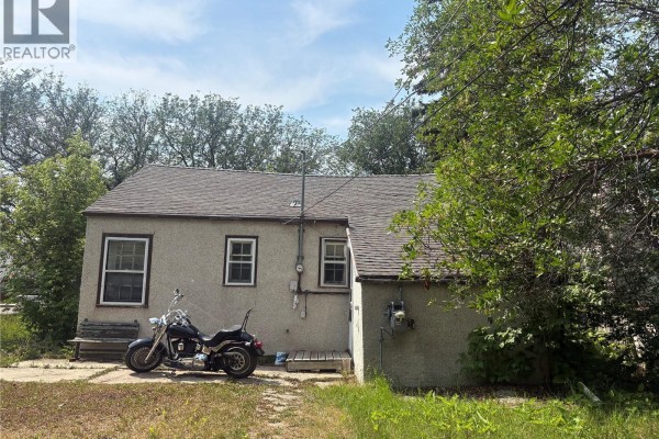 Rear exterior of the house showing a window, utility meters, and a parked motorcycle on a concrete pad. - 921 Argyle Street, Regina