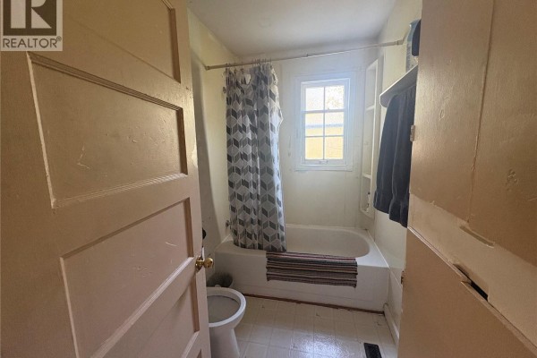 A bathroom with a white bathtub, shower curtain, toilet, and a window with natural light. - 921 Argyle Street, Regina