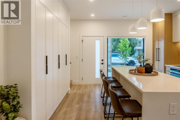 Kitchen island with pendant lights, brown stools, and an entryway with white cabinets. - 921 Borden Avenue, Kelowna