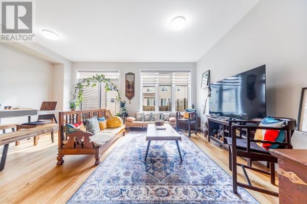 Living and dining area with hardwood floors, wooden furniture, a large rug, and windows. - 921 Clarkia Street, Ottawa