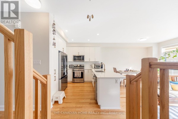 View from the stairs overlooking a modern white kitchen with stainless steel appliances and island. - 921 Clarkia Street, Ottawa
