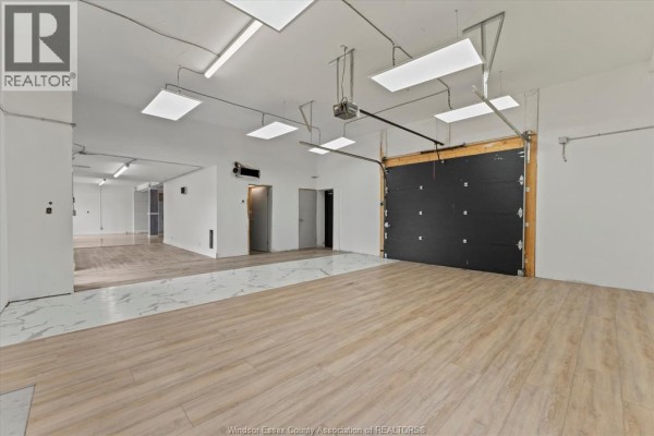 Open interior commercial space showing multiple doorways, roll-up door, and diverse flooring. - 921 Tecumseh Road West Unit# Front, Windsor