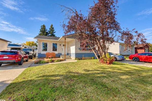 Front view of a single-family home with a wooden porch, landscaping, and vehicles parked on the driveway. - 9218 81a St, Fort Saskatchewan