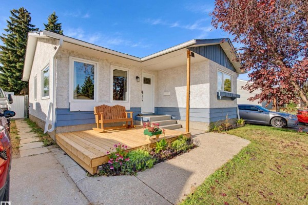 Close-up of the front entrance of a house, featuring a new wooden deck, stairs, and garden beds. - 9218 81a St, Fort Saskatchewan