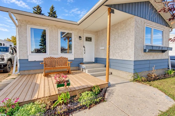 Detailed view of the house entrance with a wooden deck, white door, and stucco exterior. - 9218 81a St, Fort Saskatchewan