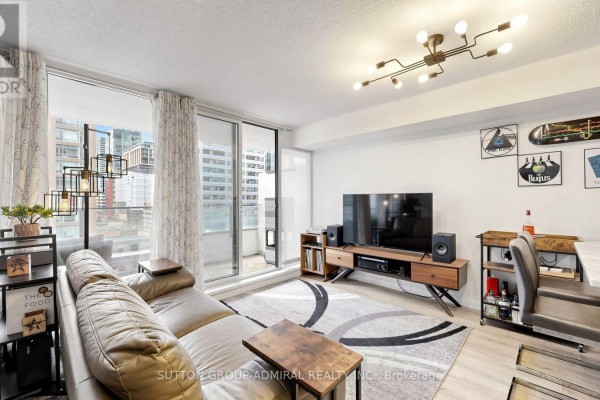Living room with a large beige sectional sofa, television, and city view through balcony doors. - 922 - 111 Elizabeth Street, Toronto