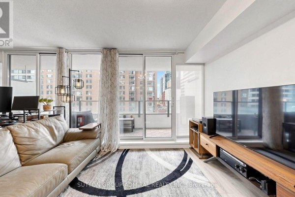 Living room with a sectional sofa, television, and view of the balcony and city skyline. - 922 - 111 Elizabeth Street, Toronto