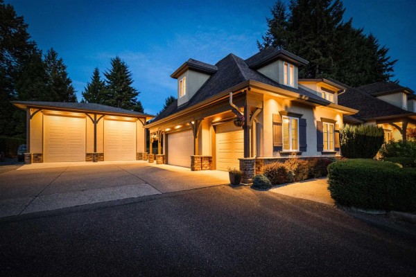 Side view of the house with a large garage and driveway, illuminated by exterior lighting at dusk. - 9228 Bodner Terrace, Mission