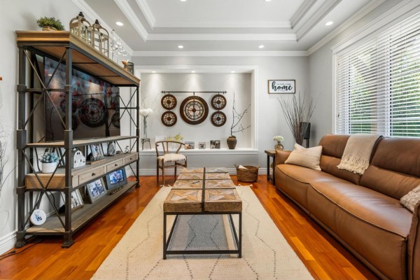 Living room with a brown leather sofa, wooden coffee table, entertainment unit, and a coffered ceiling. - 9228 Bodner Terrace, Mission