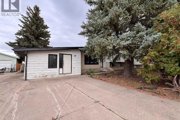 Exterior view of the house entrance and driveway, with large evergreen trees. - 924 19b Avenue, Coaldale