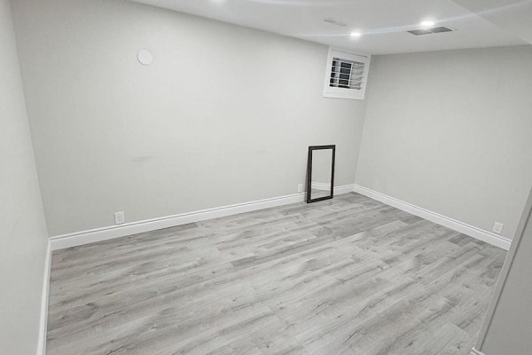 An empty room in a finished basement with light wood-look vinyl flooring and a standing mirror. - 925 Byron Street N, Whitby