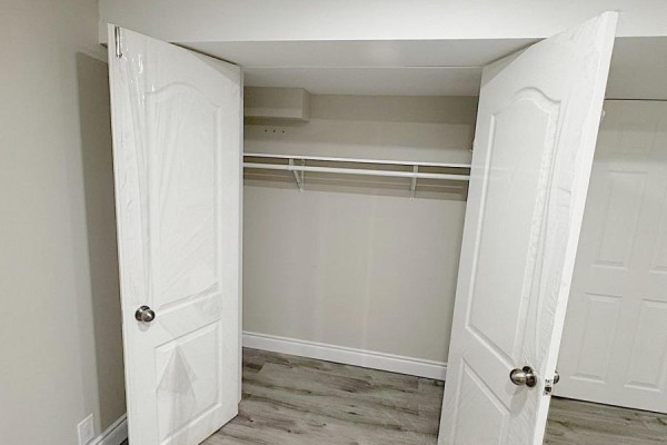 Open white bi-fold closet doors reveal a shelved closet with a hanging rod in a finished basement. - 925 Byron Street N, Whitby