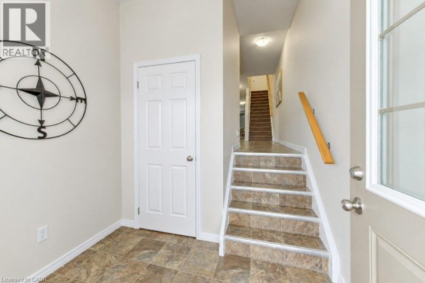 Interior entryway showing the front door, a closed door, a large compass wall decor, and carpeted stairs. - 925 Glasgow Street Unit# C, Kitchener