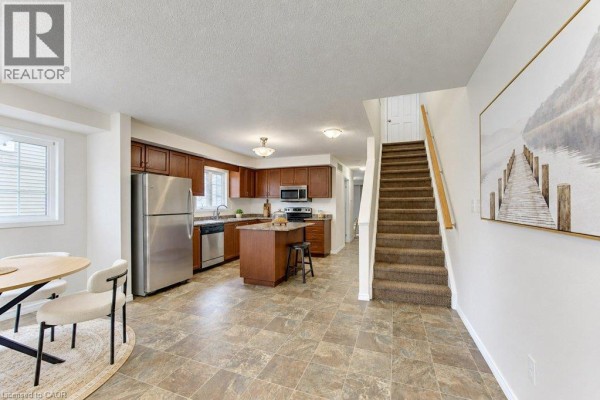Open-concept kitchen and dining area with stainless steel appliances, dark wood cabinets, and a carpeted staircase. - 925 Glasgow Street Unit# C, Kitchener