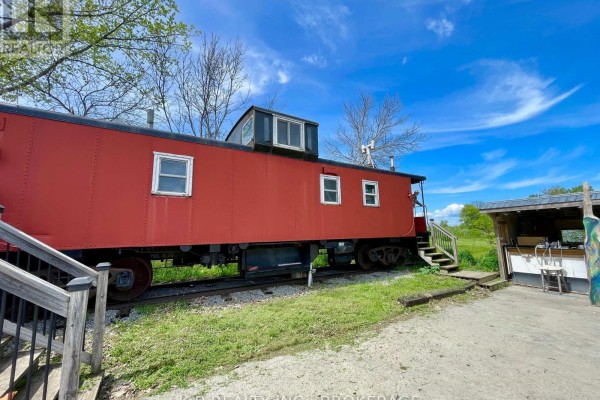 Red caboose with windows and stairs, next to an outdoor structure with a chair. - 9261 Loyalist Parkway, Greater Napanee