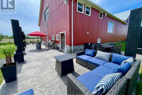 Outdoor patio seating with blue sofa and fire pit next to red barn - 9261 Loyalist Parkway Greater Napanee