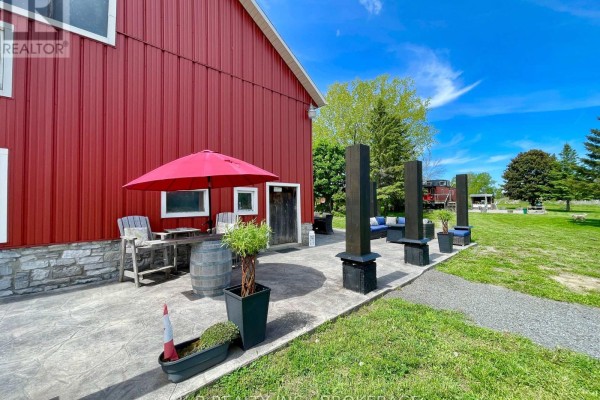 Red barn exterior with patio, seating, umbrella, and train car - 9261 Loyalist Parkway Greater Napanee