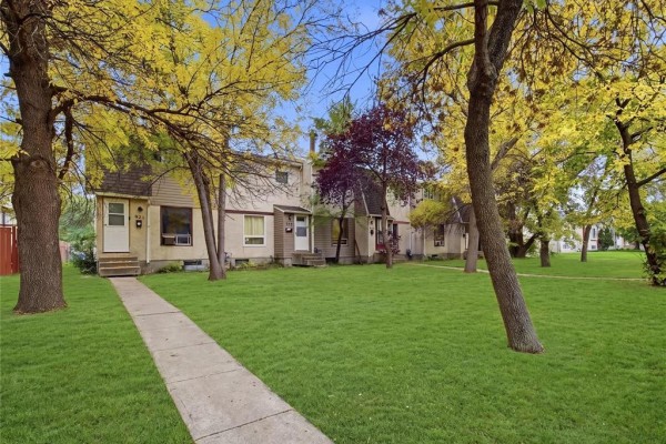 A concrete walkway leads to the entrance of a beige multi-family home with a red fence on the left. - 928 Greencrest Avenue, Winnipeg