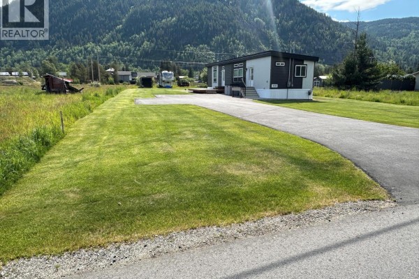 Side view of the mobile home showing gray siding, white trim, and a small wooden deck. - 928 Waterloo Crescent, Castlegar