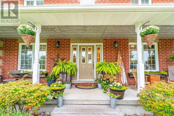 Front entrance of a red brick house with a covered porch, double doors, and hanging planters. - 929 Eldon Road, Kawartha Lakes