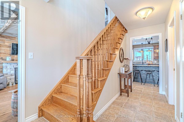 Interior hallway with a light oak staircase, tiled floor, and a view into the kitchen. - 929 Eldon Road, Kawartha Lakes