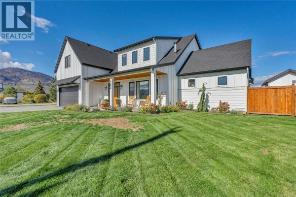 Side view of modern white farmhouse with green lawn and wooden fence on the right. - 9294 Jones Flat Road, Summerland
