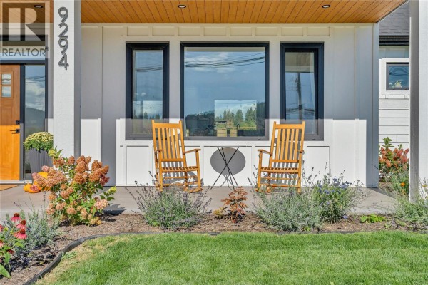 Two wooden rocking chairs and a small table on the concrete porch with garden plants. - 9294 Jones Flat Road, Summerland