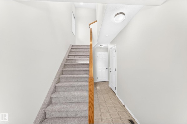 Interior view of a staircase with grey carpet, wood railing, and beige tiled floor. - #93 230 Edwards Dr Sw, Edmonton