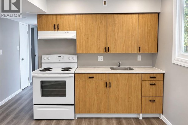 Kitchenette with light wood cabinets, white stove, stainless steel sink, and beige countertop. - 93 Brybeck Crescent Unit# C, Kitchener