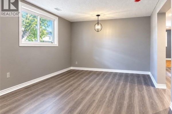 Empty room with grey walls, a modern chandelier, and a large window with trees outside. - 93 Brybeck Crescent Unit# C, Kitchener