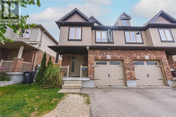 Front exterior of a townhouse with beige siding, brick lower level, and two garage doors. - 93 Couling Crescent, Guelph