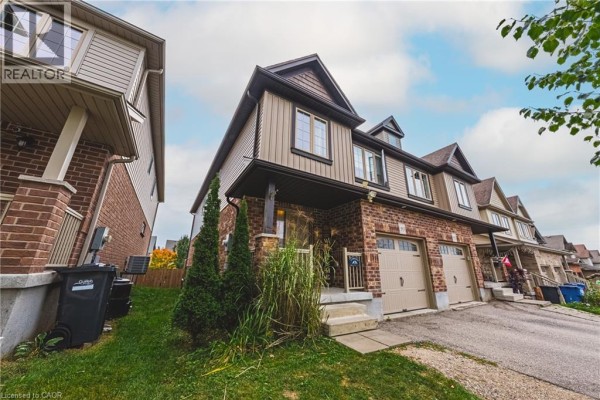 Side view of a townhouse exterior showcasing brick and beige siding, porch, and garage doors. - 93 Couling Crescent, Guelph