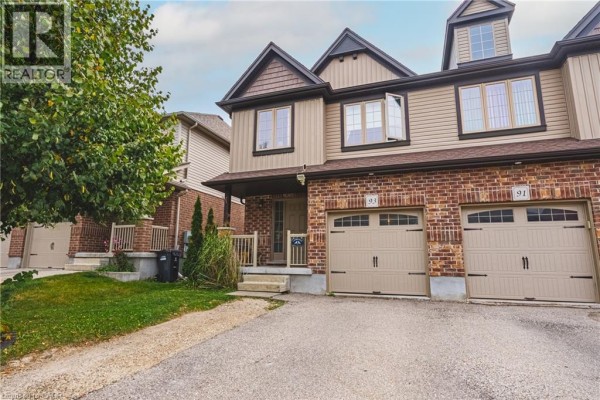Street view of a townhouse complex with beige siding, brick detailing, and garage doors. - 93 Couling Crescent, Guelph