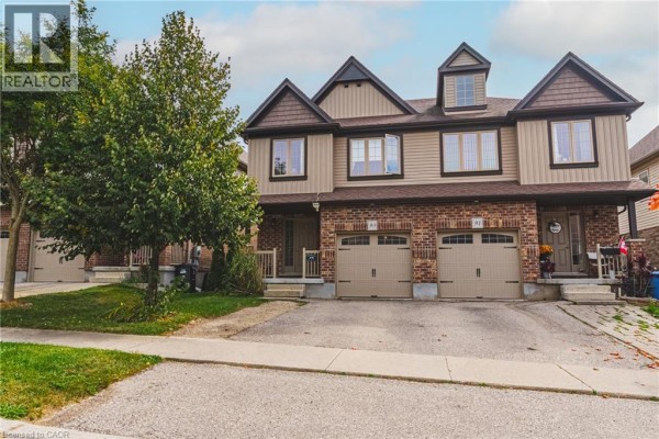 Exterior of a townhouse complex with beige siding, brick accents, and multiple garage doors. - 93 Couling Crescent, Guelph