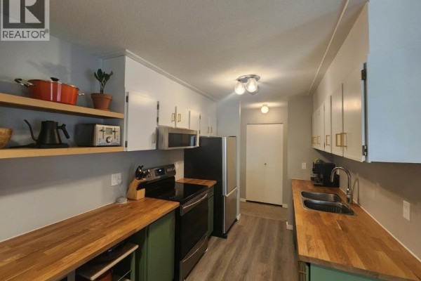 Kitchen with white cabinets, wooden countertops, stainless steel appliances, and a hallway. - 93 Deerborne Drive Unit# 102, Elkford