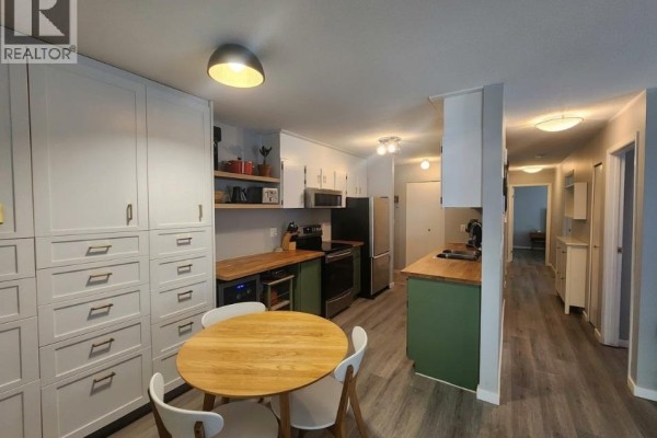 View of the kitchen, dining area, and hallway with white cabinets and wooden countertops. - 93 Deerborne Drive Unit# 102, Elkford
