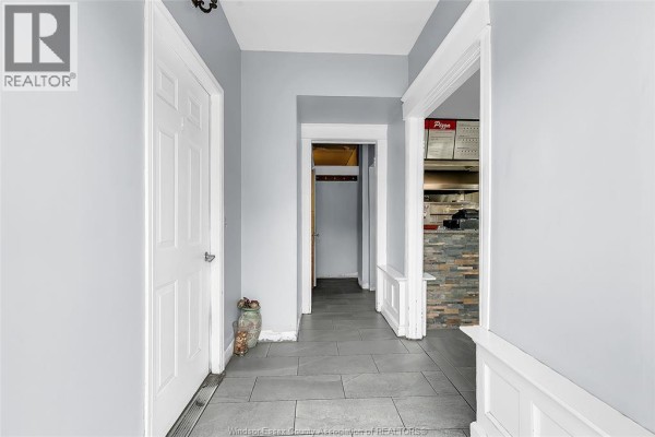 Interior hallway with light grey walls, white doors, tile floor, and entryway to a kitchen area. - 93 Erie Street South, Leamington