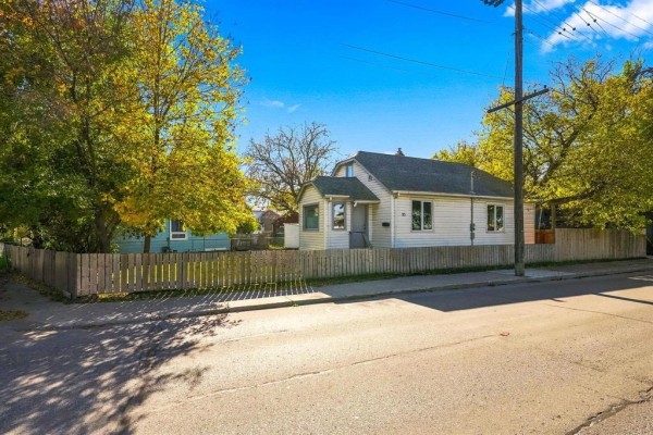 Side exterior view of the white house with surrounding trees and sidewalk. - 93 Gateway Road, Winnipeg