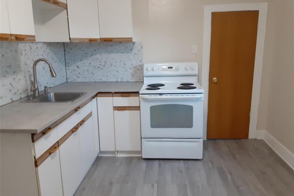 Close-up of a white kitchen with grey flooring, white cabinets, and a white stove. - 93 Gateway Road, Winnipeg