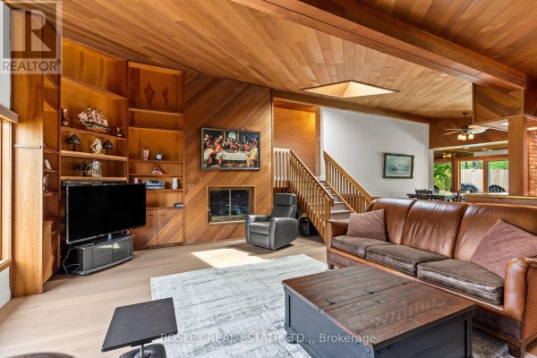 Living room with floor-to-ceiling wood paneling, a brick fireplace, leather sofa, and built-in bookshelves. - 93 Riverview Boulevard, St  Catharines