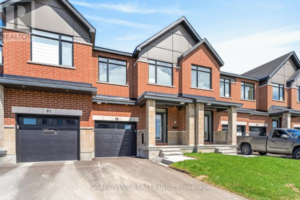 Front exterior of townhouses with red brick facades, stone accents, and dark garage doors. - 93 San Felice Circle, Ottawa