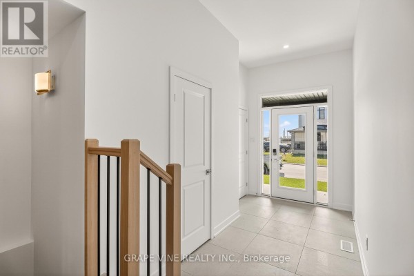 Interior hallway with light grey tiled floor, white walls, wooden staircase with black spindles, and glass front doors. - 93 San Felice Circle, Ottawa