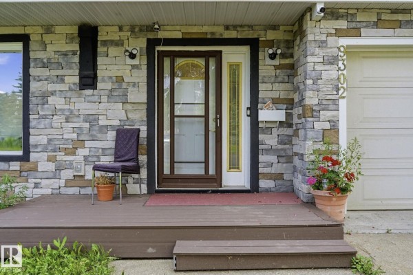Close-up of the front porch entrance, featuring a wooden deck, glass door, and stone exterior. - 9302 165 St Nw, Edmonton