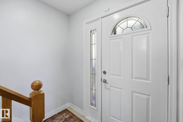 Interior view of a white front door with a glass pane above, next to a staircase. - 9302 165 St Nw, Edmonton