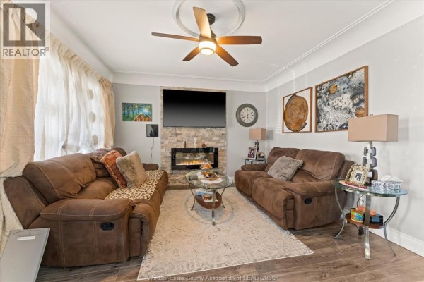 Living room with two brown reclining sofas, a stone-faced fireplace, and a ceiling fan. - 931 Lillian Avenue, Windsor
