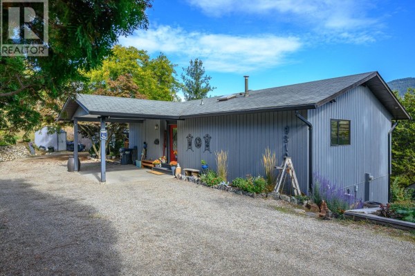 Exterior view of the grey sided home with a red front door and covered carport area. - 9310 Northcott Drive, Coldstream