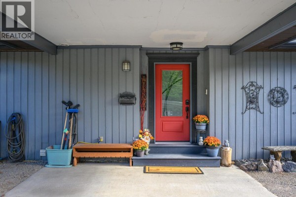 Close-up of the red front door, porch, and covered entryway of the grey siding house. - 9310 Northcott Drive, Coldstream