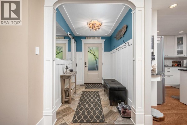 Interior entrance hallway with white wainscoting, blue walls, a red door, and a bench. - 9310 Northcott Drive, Coldstream